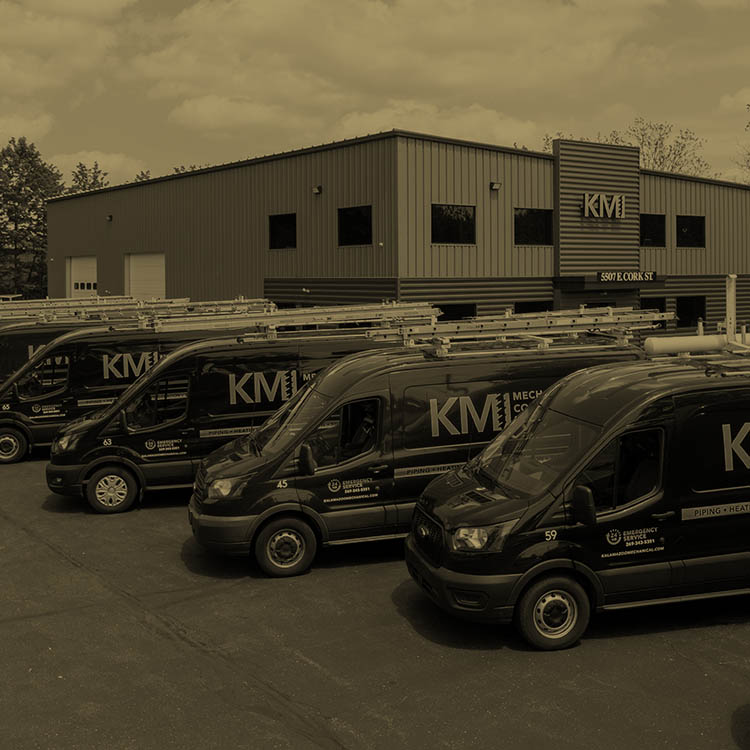 Service vehicles parked diagonally in a row outside of the KMI - Kalamazoo Mechanical building.