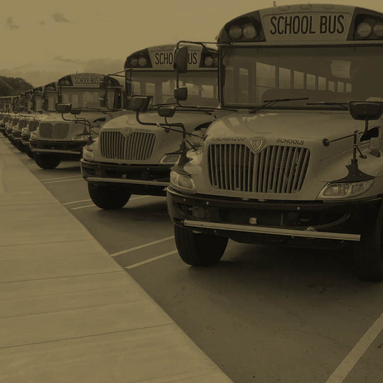 A row of buses parked diagonally in the parking lot of Kalamazoo Public School's bus fleet facility.