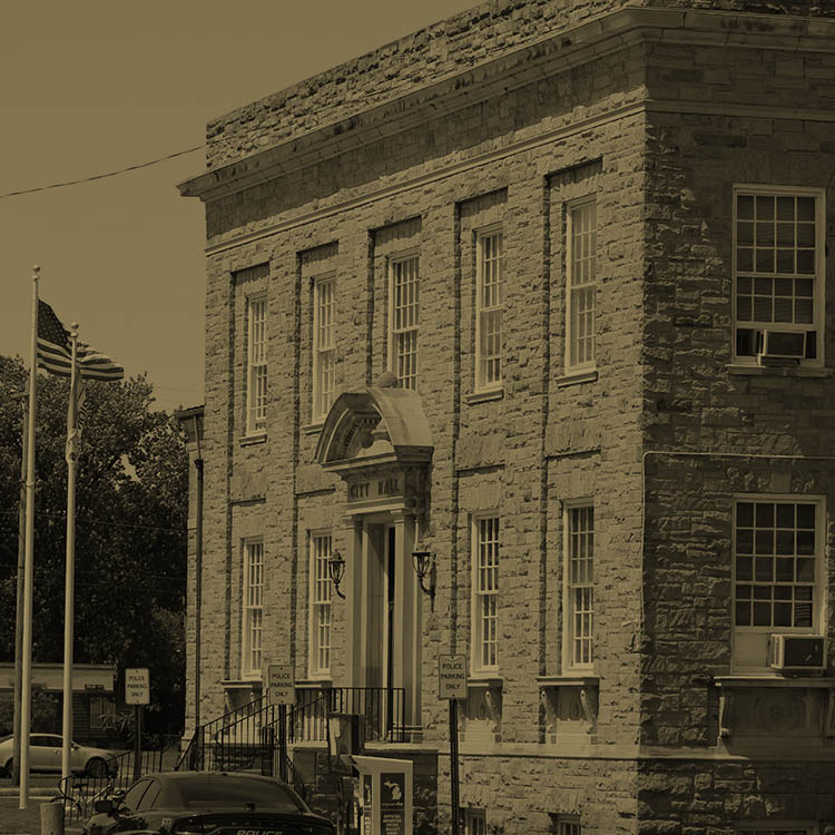 Front of city hall on a sunny day with flags on a flagpole next to the building.